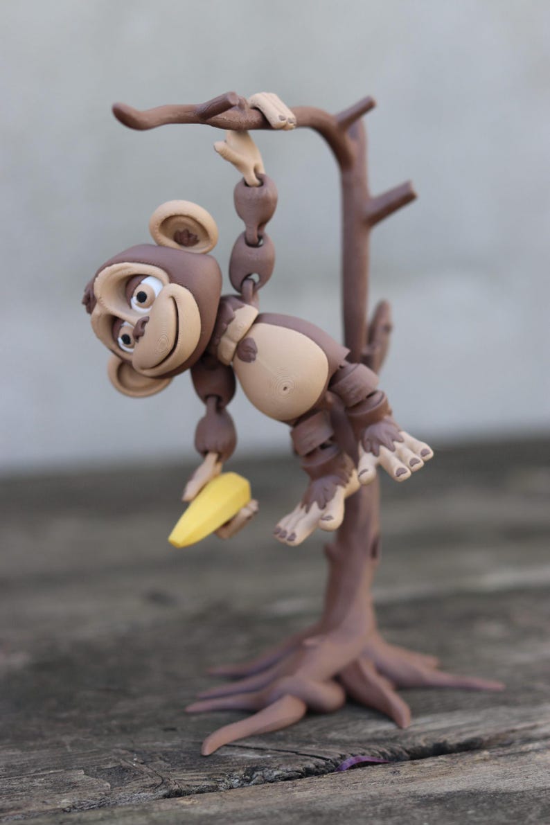 May include: A brown monkey figurine holding a yellow banana, hanging from a brown tree branch with a brown base.