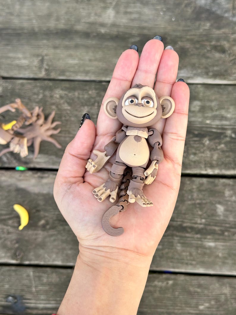 May include: A brown articulated monkey toy with a smiling face and a long tail. The monkey is posed with its arms outstretched and its legs bent. The toy is made of plastic and has a realistic appearance.