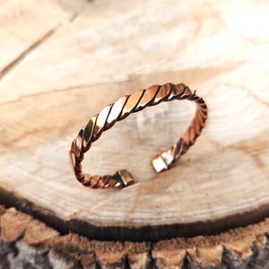 May include: A copper bracelet with a twisted design. The bracelet is open and has a magnetic clasp.