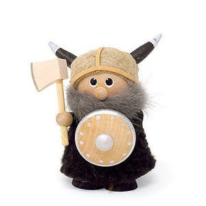 May include: A wooden figurine of a Viking warrior wearing a brown helmet with horns, a black fur cloak, and holding a wooden axe and shield.
