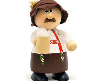 May include: A wooden figurine of a person wearing a brown hat and white shirt with a red sash. The person is holding a brown mug with a white foam top.