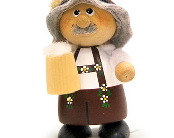 May include: A wooden figurine of a person wearing a gray hat and holding a beer stein. The figurine is painted with brown, white, and green details.