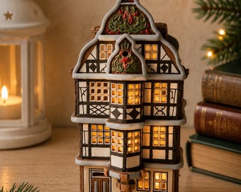 Puede incluir: Una figura de casa en miniatura de cerámica con estilo arquitectónico de entramado de madera, vigas negras, paredes blancas y múltiples ventanas iluminadas. La estructura tiene un mirador central y un tejado a dos aguas con detalles.