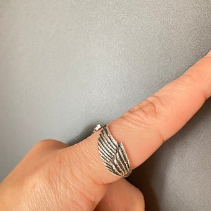 May include: A silver ring with a wing design. The ring is adjustable and can be worn on any finger.