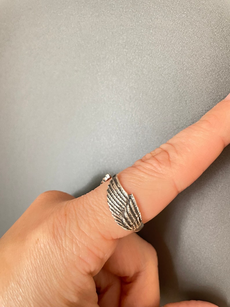 May include: A silver ring with a wing design. The ring is adjustable and can be worn on any finger.