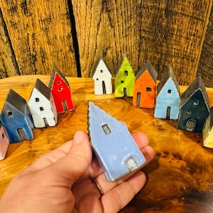 May include: A collection of small, hand-painted ceramic houses in various colors, including blue, green, red, and pink. The houses are arranged in a semi-circle on a wooden surface.