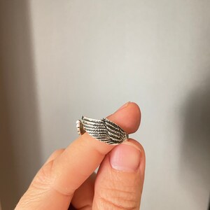 May include: A silver ring with a wing design. The ring is on a finger.
