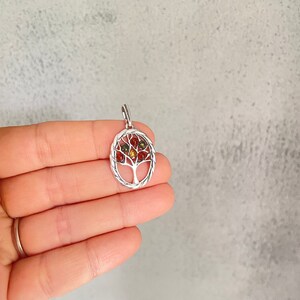 May include: A silver tree of life pendant with red, orange, and green gemstones. The pendant is on a white background.