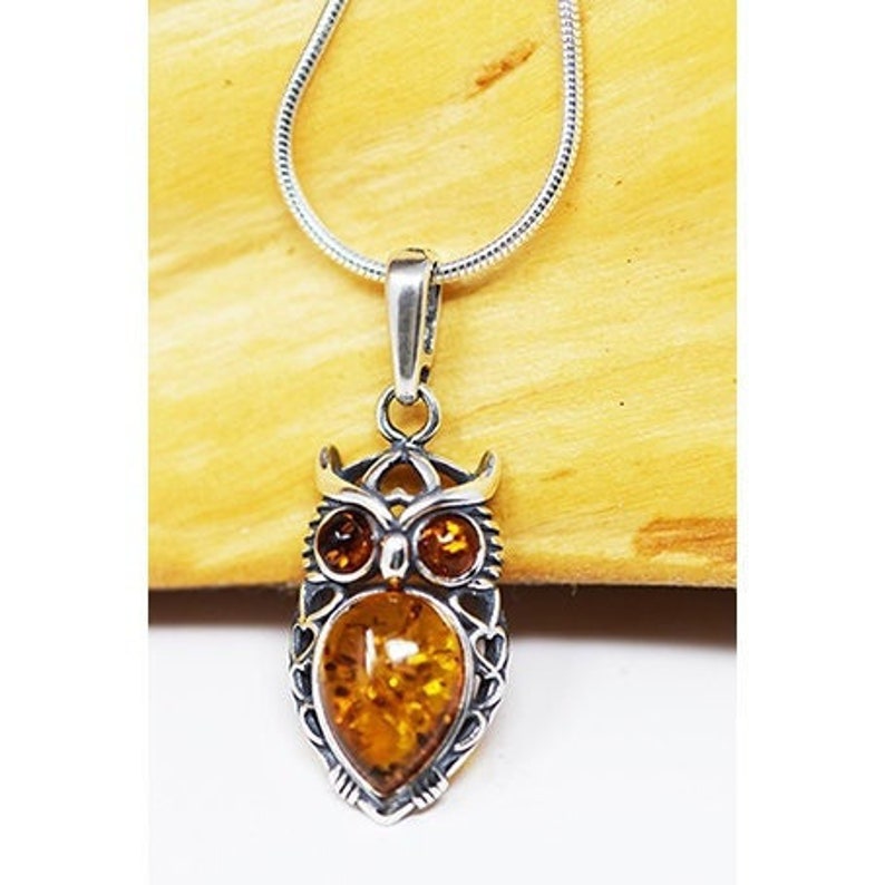 May include: Silver owl pendant necklace with an intricate design. The pendant has a large amber-coloured stone at its centre, with smaller amber stones for eyes. The necklace has a delicate silver chain.