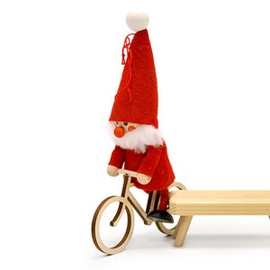 May include: A red and white Santa Claus figurine riding a wooden bicycle with a wooden bench.