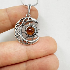 May include: A silver pendant necklace featuring a crescent moon design with Celtic knotwork and a sunburst. The sun in the center is a round amber stone. The necklace has a silver chain.