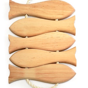 May include: Set of five wooden fish-shaped trivets connected by a white rope. The trivets are made of light brown wood and have a natural wood grain.
