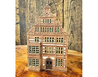 May include: A detailed miniature replica of a brown brick building with white trim and green windows. The building has a gabled roof and a decorative facade.