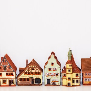May include: A collection of six miniature ceramic houses with brown, yellow, and green paint. The houses have intricate details, including windows, doors, and roofs. The houses are arranged in a row on a white surface.