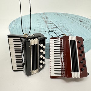 May include: Two miniature accordion ornaments, one black and one brown, with white keys and black bellows. Both have a black string for hanging.