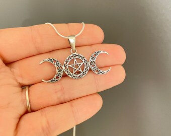 May include: Silver necklace with a triple moon pendant featuring a pentagram in the center. The pendant is detailed with intricate knotwork.