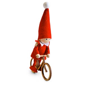 May include: A red felt elf doll riding a wooden bicycle with white wheels. The elf has a white pom-pom hat and a white collar.