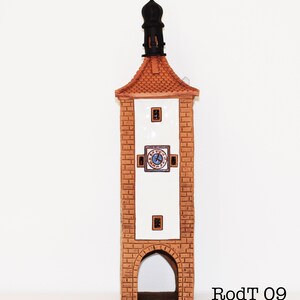 May include: A ceramic tower with a clock face and a pointed roof. The tower is brown and white with a black roof. The clock face has Roman numerals and a blue background. The tower is labeled "RodT 09".