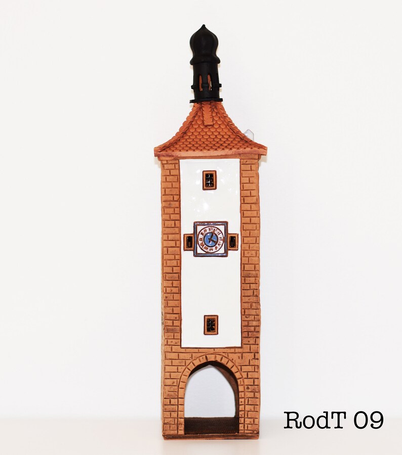 May include: A ceramic tower with a clock face and a pointed roof. The tower is brown and white with a black roof. The clock face has Roman numerals and a blue background. The tower is labeled "RodT 09".