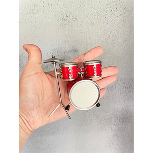May include: A miniature red drum kit with a cymbal and stand. The drum kit is made of metal and has a silver finish.