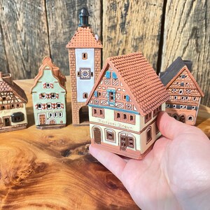 May include: Five miniature ceramic houses with brown, green, and white paint. The houses have detailed facades and roofs. One house has the text "Hotel Braun" on the front.