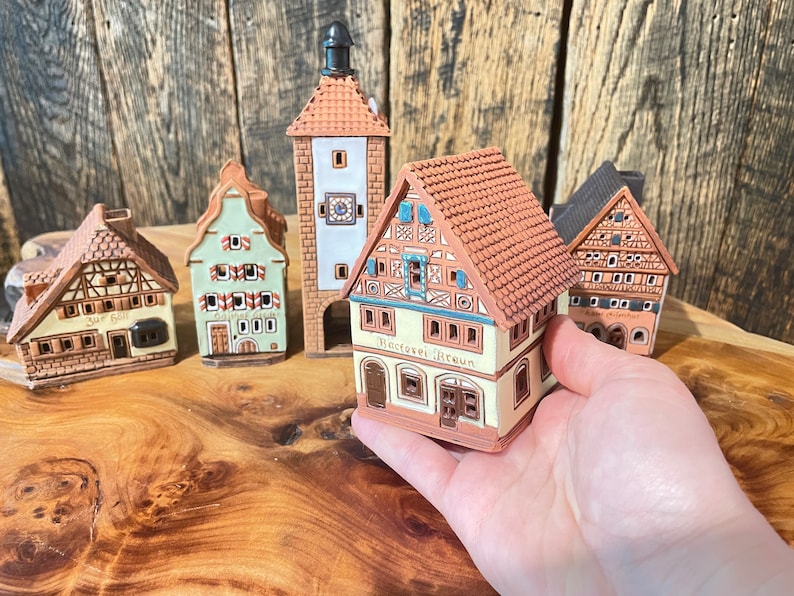 May include: Five miniature ceramic houses with brown, green, and white paint. The houses have detailed facades and roofs. One house has the text "Hotel Braun" on the front.