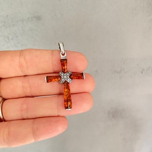 Puede incluir: Un colgante de cruz de plata con una incrustaci&oacute;n de piedra &aacute;mbar marr&oacute;n y un peque&ntilde;o acento de diamante.
