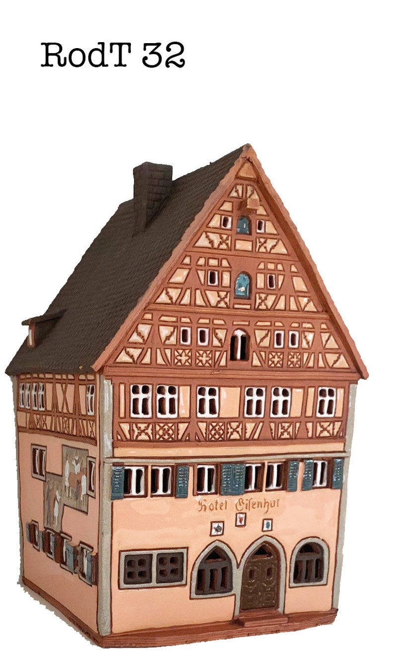 May include: A ceramic model of a traditional German building with a brown roof, white trim, and a sign that reads "Hotel Gifenhur". The building has a half-timbered facade and is decorated with intricate details.