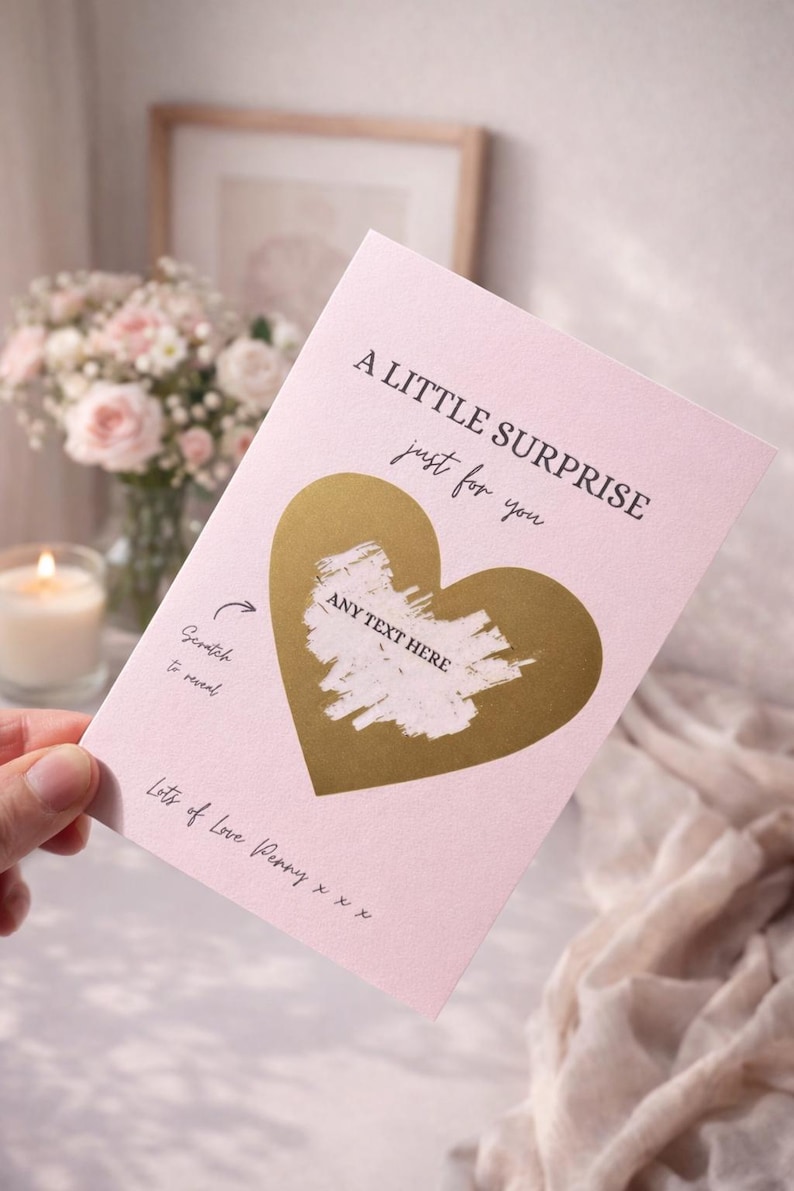 Puede incluir: Una tarjeta rosa para rascar con un coraz&oacute;n dorado y el texto "A LITTLE SURPRISE just for you". La tarjeta tiene el texto "Scratch to reveal" y "ANY TEXT HERE". La tarjeta est&aacute; sujeta en una mano.