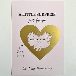 Puede incluir: Tarjeta rosa con el texto "A LITTLE SURPRISE just for you". Un coraz&oacute;n dorado para rascar en el centro, con "ANY TEXT HERE" encima. La parte inferior dice "Lots of Love Penny x x x." Instrucciones "Scratch to reveal."