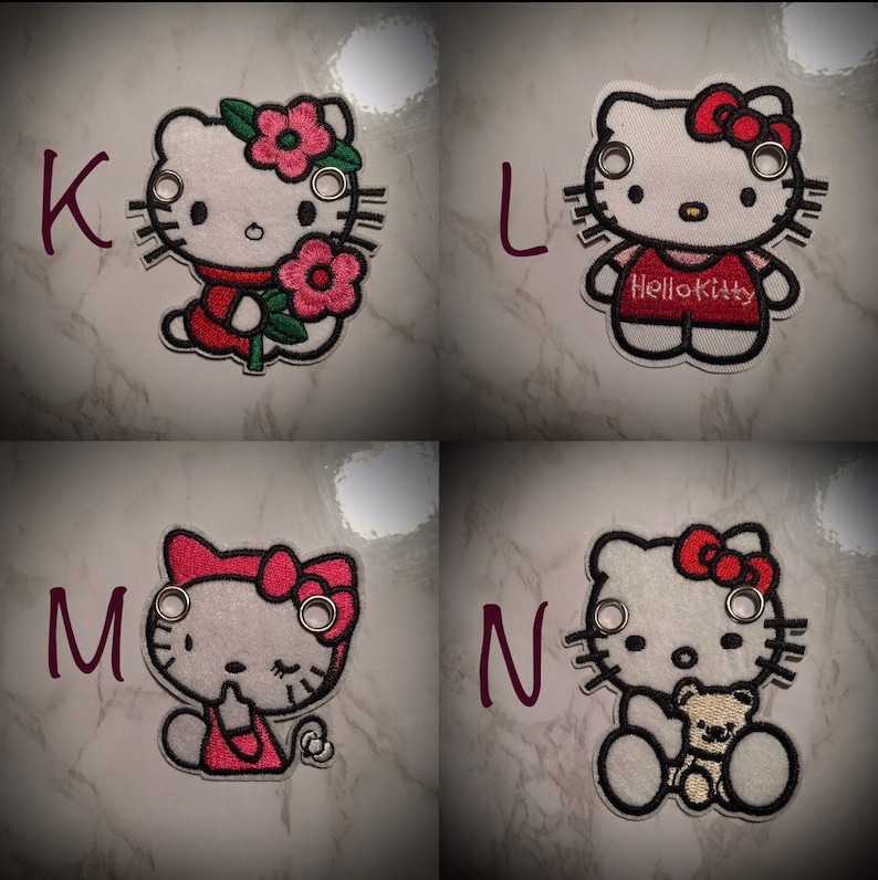 May include: Four embroidered patches featuring Hello Kitty in different poses. The patches are white with red and black details. The first patch shows Hello Kitty holding a flower. The second patch shows Hello Kitty wearing a red shirt with the text "Hello Kitty". The third patch shows Hello Kitty with her eyes closed. The fourth patch shows Hello Kitty holding a teddy bear.