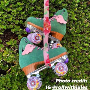 May include: A pair of green roller skates with pink wings and floral patterned straps. The wheels are yellow with purple accents and the words "Fundae" are printed on the wheels.