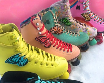 May include: Five pairs of roller skates with butterfly charms on the laces. The skates are in various colors, including yellow, pink, green, and brown. The butterflies are in different colors and patterns.