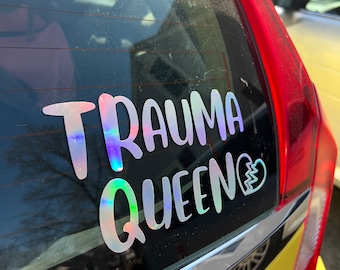 Może przedstawiać: Tylna szyba żółtego samochodu z białym naklejką winylową z napisem "Trauma Queen" i symbolem złamanego serca. Naklejka ma holograficzne, tęczowe wykończenie.