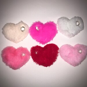 May include: Six plush heart-shaped keychains in various colors: white, pink, light pink, red, and a darker pink. Each keychain has a silver ring attached.