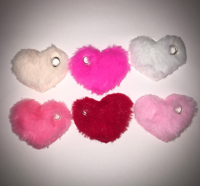 May include: Six plush heart-shaped keychains in various colors: white, pink, light pink, red, and a darker pink. Each keychain has a silver ring attached.