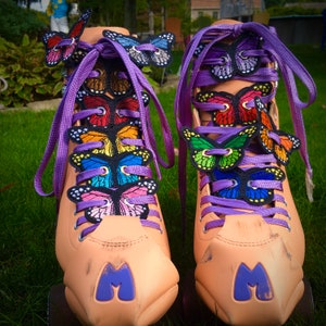 Peut inclure: Une paire de patins &agrave; roulettes avec des lacets violets et des appliques en forme de papillon. Les patins sont de couleur brun clair et ont un "M" violet sur le devant.