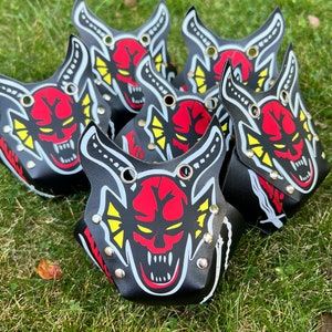 May include: Six black leather wrist cuffs with red, yellow, and white devil face designs. Each cuff has multiple silver eyelets.