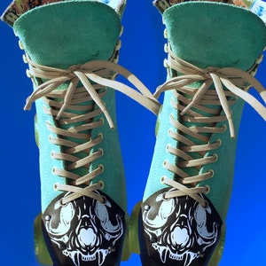 May include: A pair of teal blue roller skates with black wheels and white skull-shaped toe guards. The skates have tan laces and a colorful patterned lining.