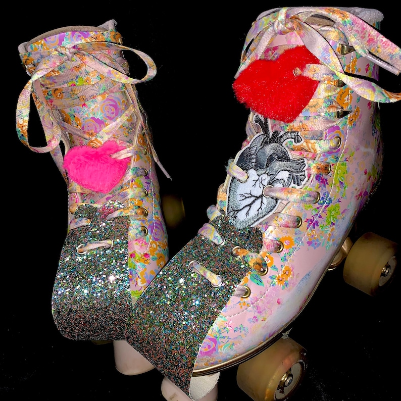 May include: A pair of pink roller skates with floral print and glitter accents. The skates have red and pink heart-shaped charms and a black and white anatomical heart patch.