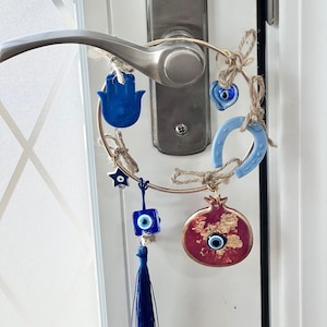 May include: A gold hoop with blue and red evil eye charms, a blue hamsa hand, a blue horseshoe, a blue star, a blue evil eye charm with a tassel, and a red pomegranate with a gold evil eye charm.