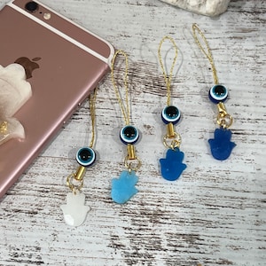 May include: Four gold phone charms with blue evil eye beads and blue and white hamsa hand charms. The charms are hanging from gold chains.