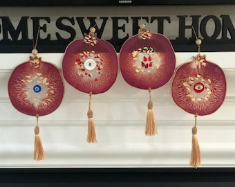 May include: Four decorative pomegranate ornaments with a deep red hue, featuring gold accents and eye-shaped designs. Each ornament has a tassel and a gold string for hanging. The background includes the text "HOME SWEET HOME".