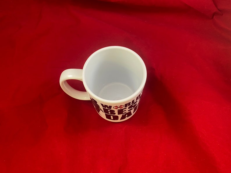 A top-down view of a mug inspired by the RE universe, specifically Village, with the words World's Best Dad in stylized caps, along with a silhouette of the main character.