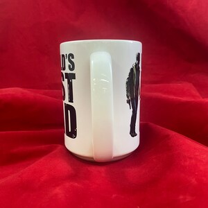 Handle view of a coffee mug inspired by the RE universe, specifically Village, with the words World's Best Dad in stylized caps, along with a silhouette of the main character.