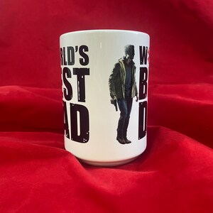 A front view of a mug inspired by the RE universe, specifically Village, with the words World's Best Dad in stylized caps, along with a silhouette of the main character.