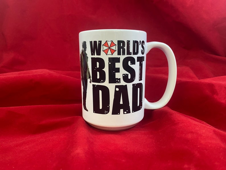 A two-sided mug inspired by the RE universe, specifically Village, with the words World's Best Dad in stylized caps, along with a silhouette of the main character.