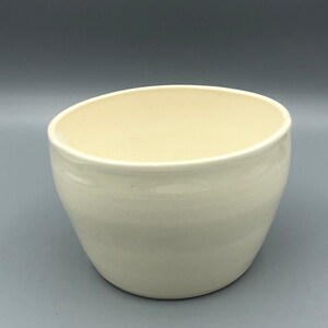 Peut inclure: Bol en céramique de couleur crème avec un bord légèrement asymétrique. Le bol a une finition lisse et brillante et un design simple et élégant. L'intérieur est d'une nuance de crème plus claire.