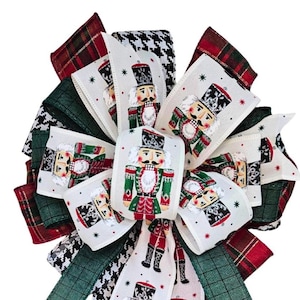 May include: A decorative Christmas bow featuring a festive design. The bow incorporates various ribbons with patterns like plaid, houndstooth, and a repeating image of a nutcracker soldier. The color palette includes red, green, white, and black.