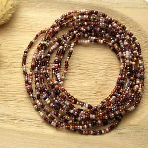 Op de afbeelding: Een meerstrengs kralenketting met een mix van bruine, roze en witte kralen. De kralen zijn klein en uniform in grootte, wat een delicate en ingewikkelde uitstraling creëert.